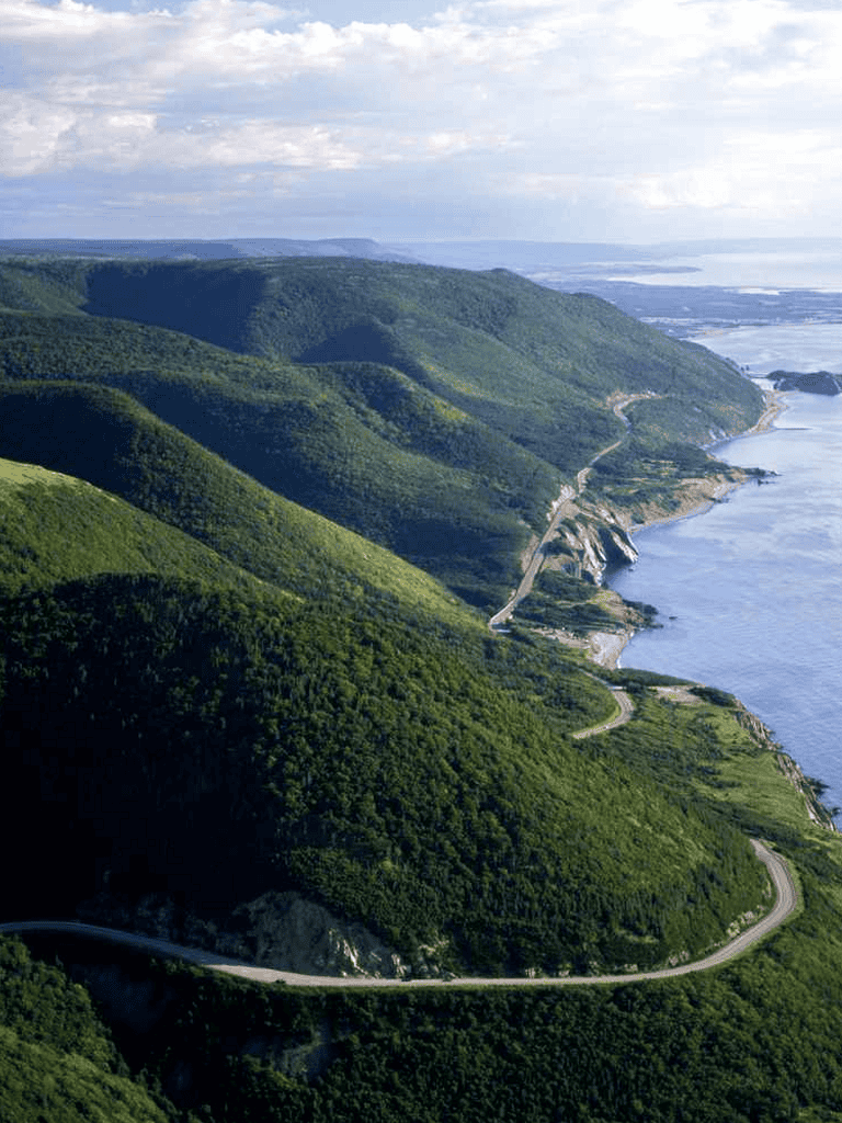 Lush coastal mountain scenery with winding road along the shoreline, scenic nature travel destination.