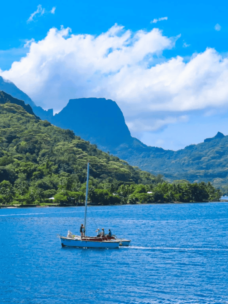 Serene tropical landscape with sailing boat on clear blue water, lush green mountains, and cloudy sky, perfect for travel and adventure.