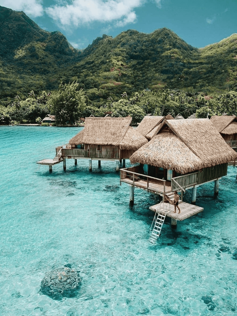 Overwater bungalows in crystal-clear turquoise waters with lush tropical mountains in the background.