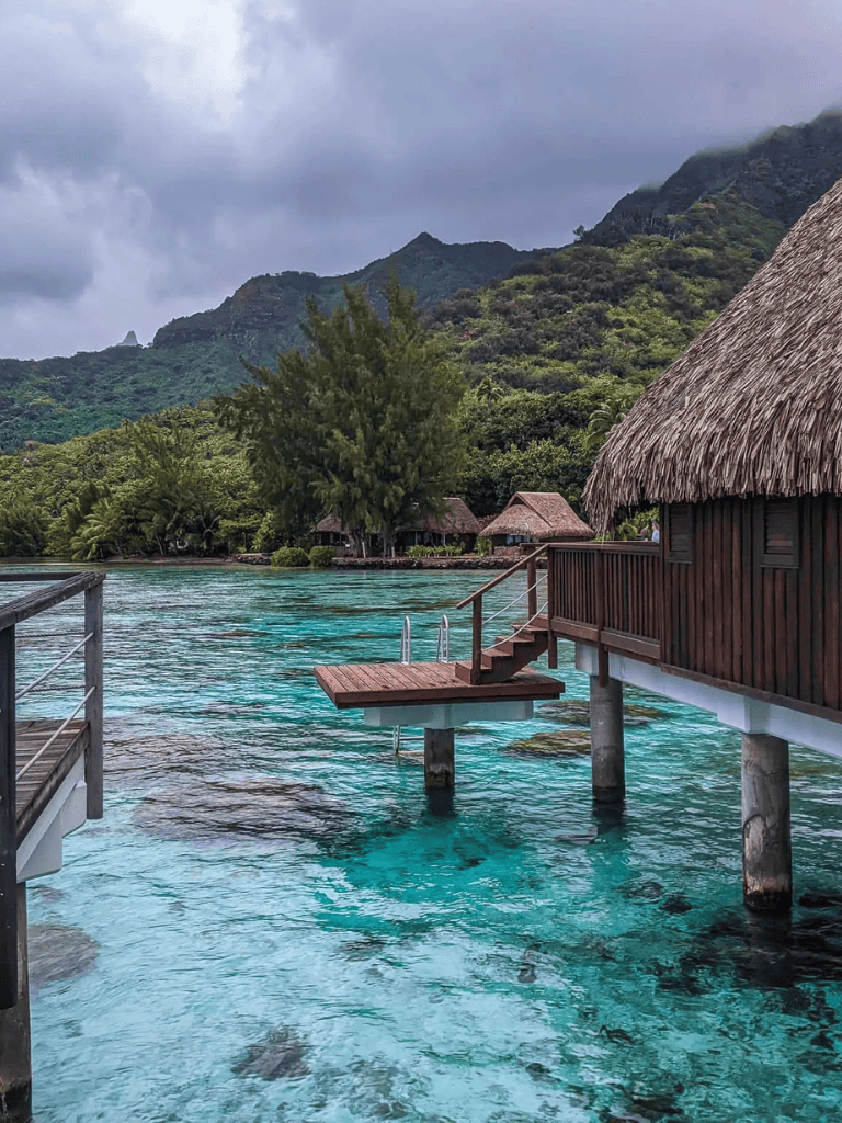 Overwater bungalow in tropical paradise with lush mountains and turquoise waters.