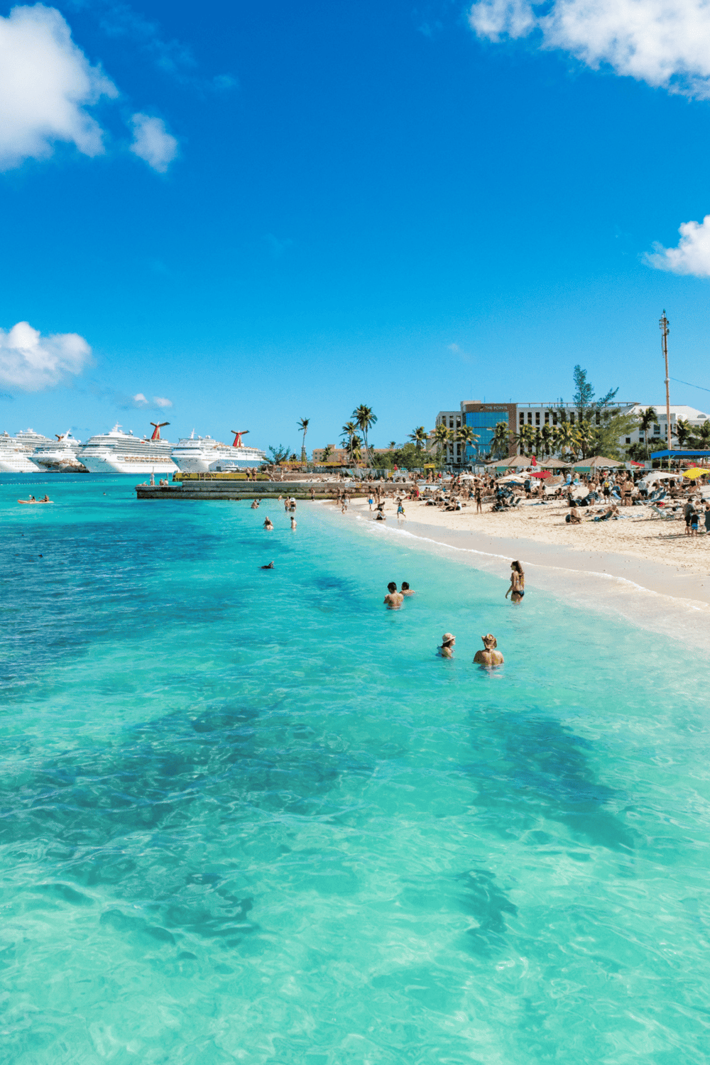 Cruise ships at sunny beach with travelers enjoying turquoise waters and white sand.