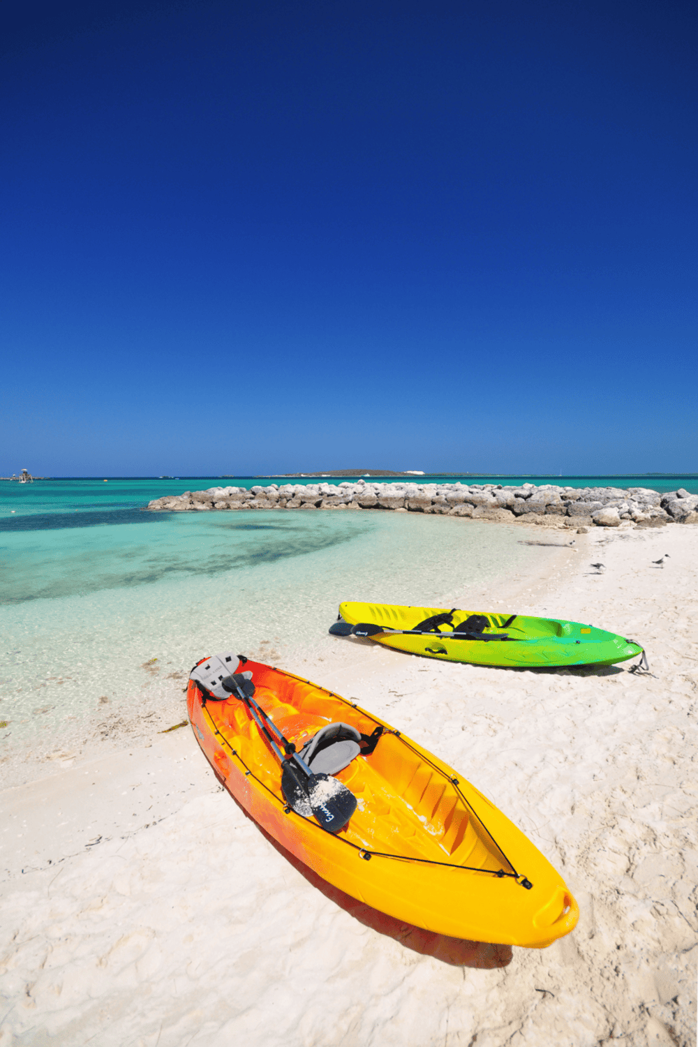 Bright yellow and green kayaks on a sandy beach with turquoise water and clear blue sky, perfect for outdoor water activities.