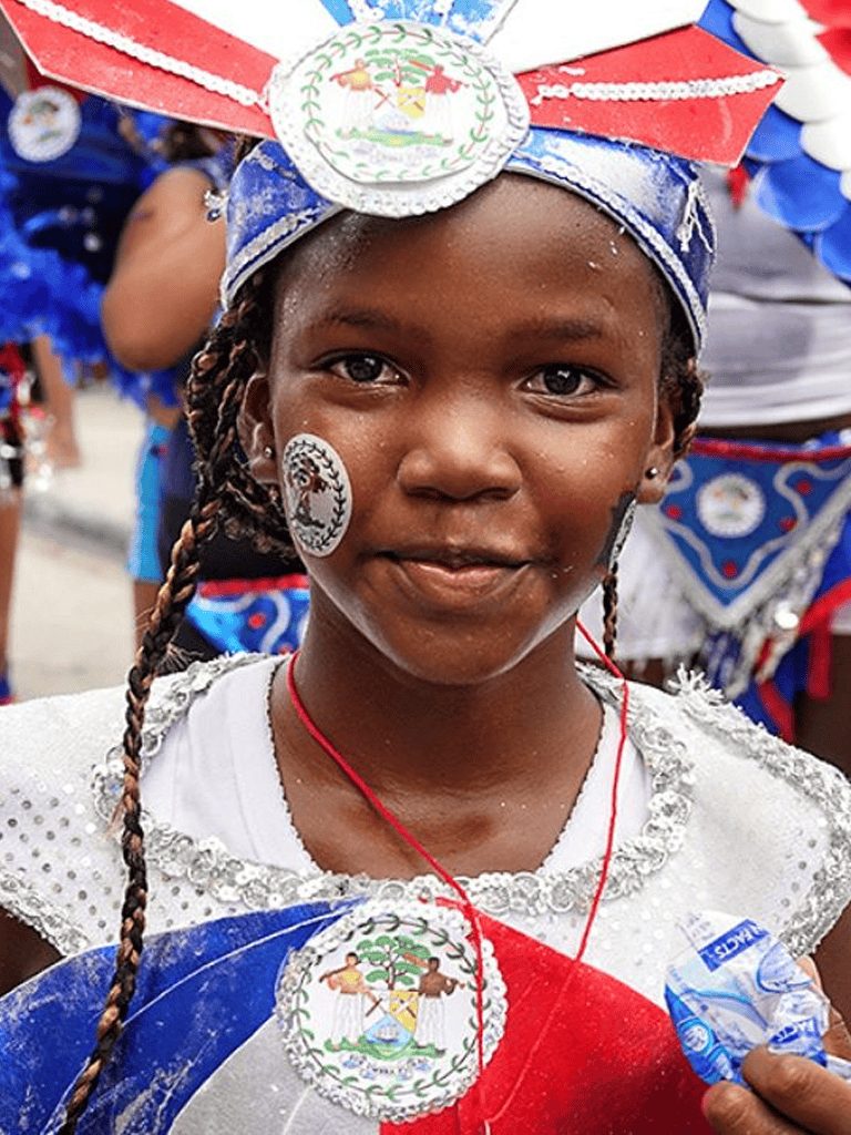Colorful Haitian girl wearing traditional attire for Haiti Flag Day celebration, smiling at the parade.