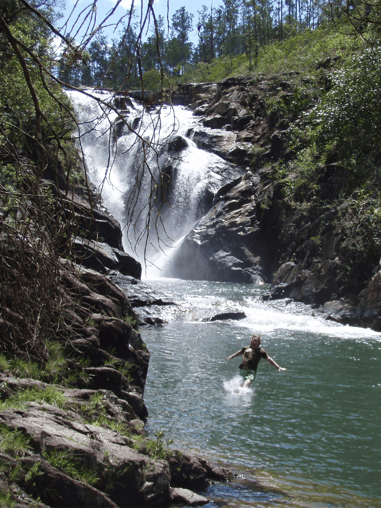 Vancouver waterfall with a child swimming, surrounded by lush trees, scenic nature, and rocky landscape.