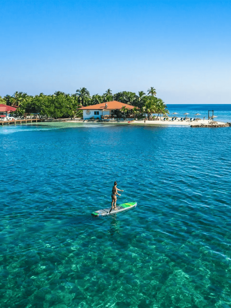 Vibrant tropical waters with paddleboarding and beachfront resort scene.