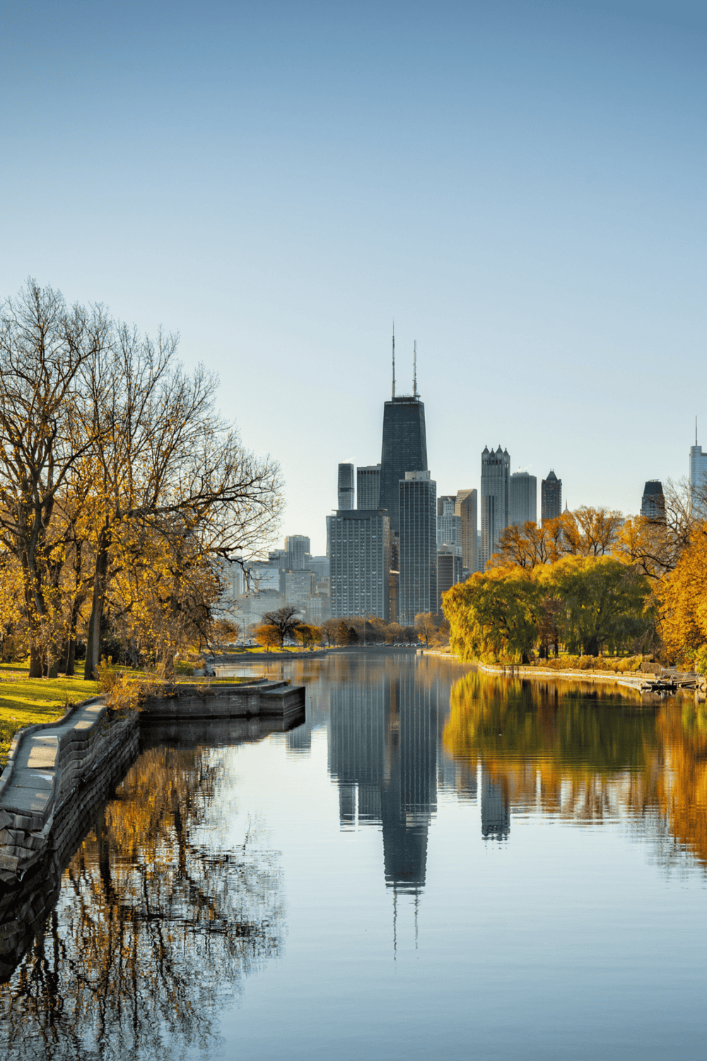 Chicago skyline with autumn trees reflecting on the water, in a scenic city park.