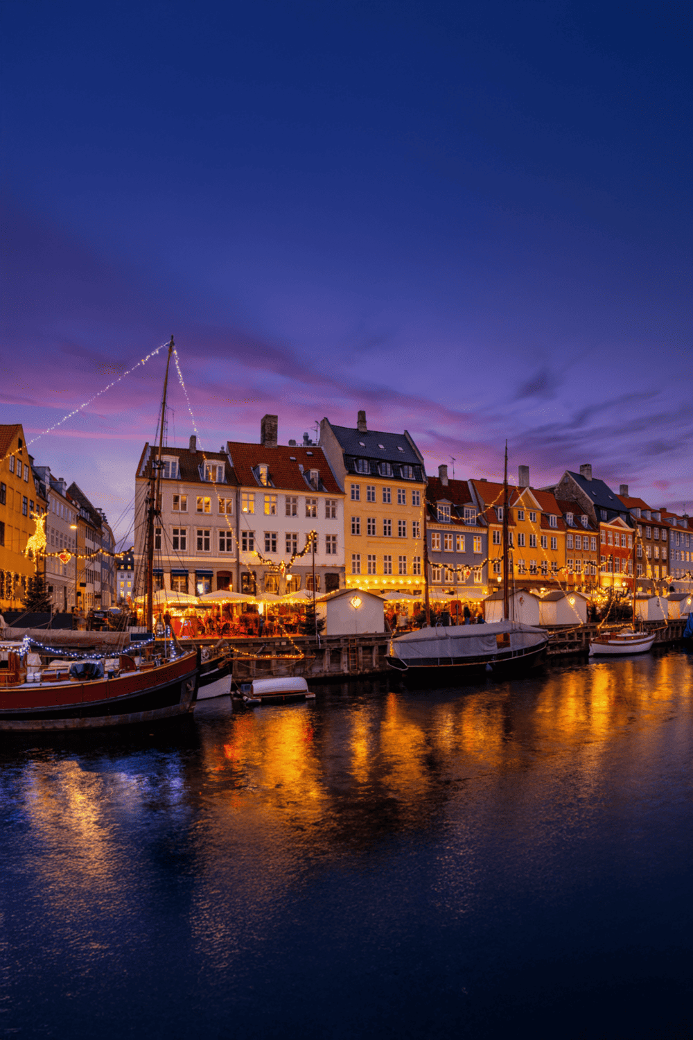 Colorful waterfront cityscape at dusk with illuminated buildings and boats in the harbor, showcasing travel and navigation.