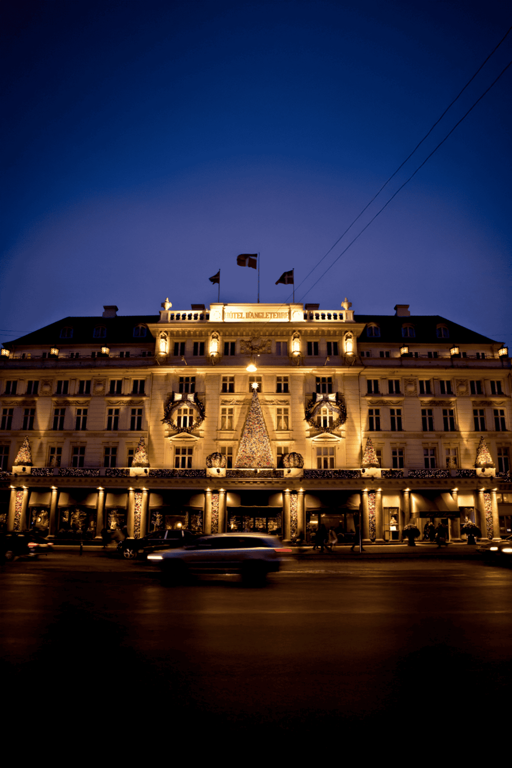 Elegant historic hotel illuminated at night with festive holiday decorations and Christmas trees.