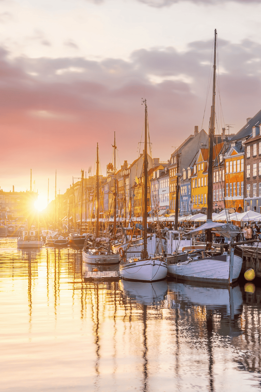Picturesque harbor with colorful buildings and sailboats at sunset, perfect for exploring Copenhagen.