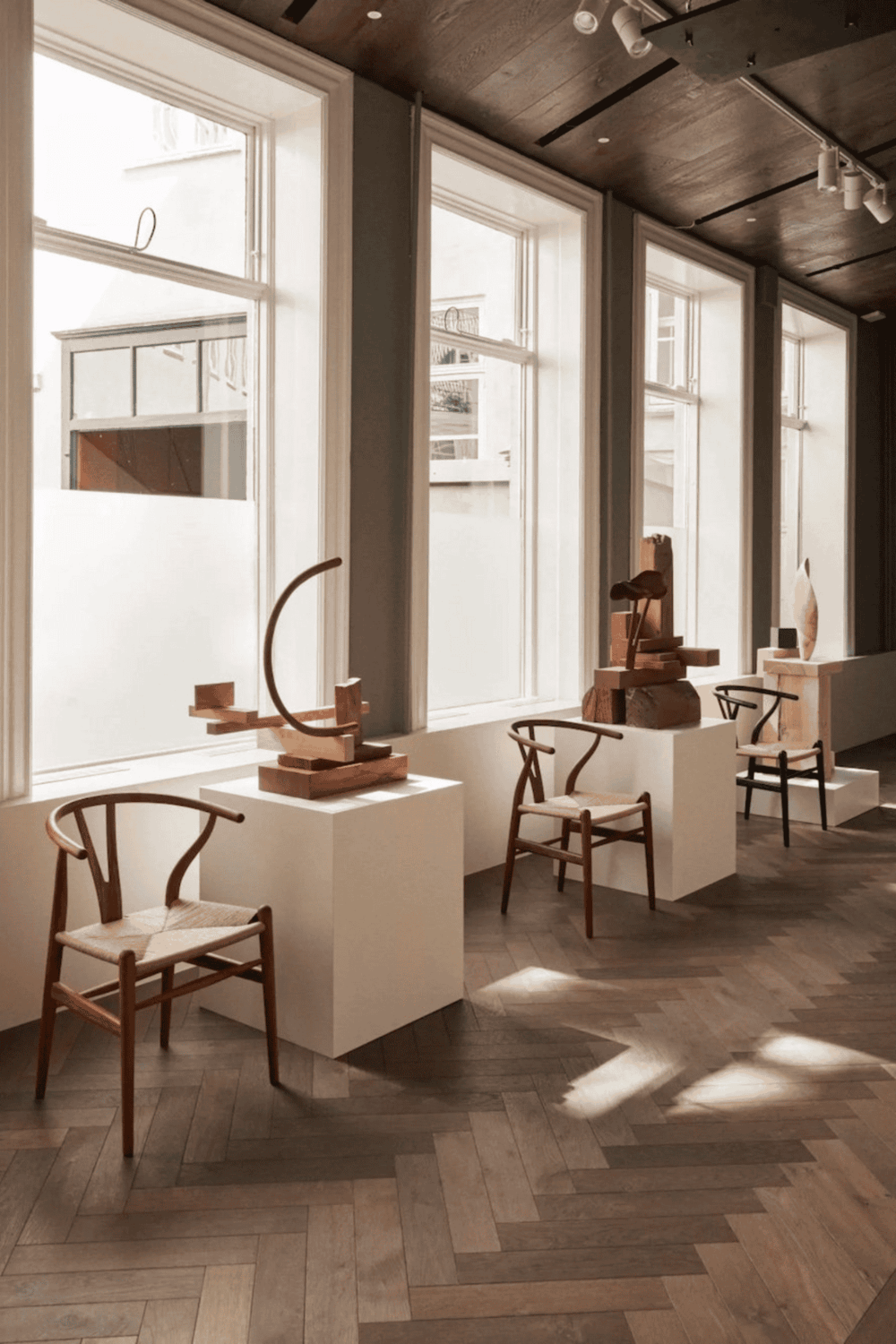 Elegant modern interior with natural light, showcasing wooden chairs and abstract sculptures.