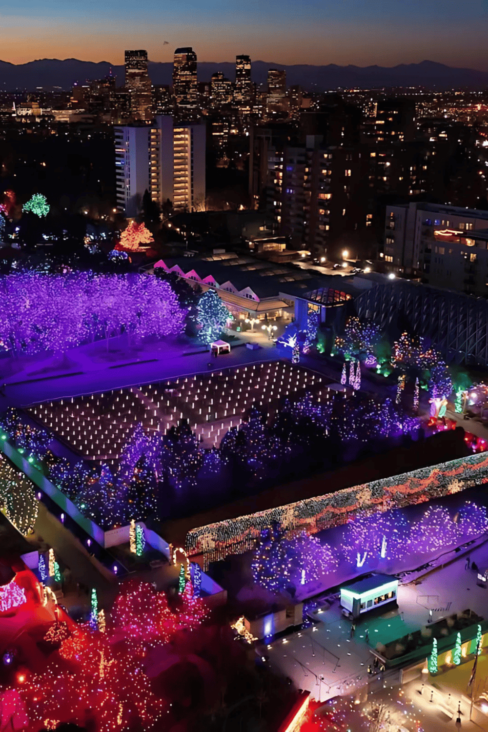 Colorful holiday lights illuminating a city park and skyline at dusk, showcasing festive decorations and urban charm.