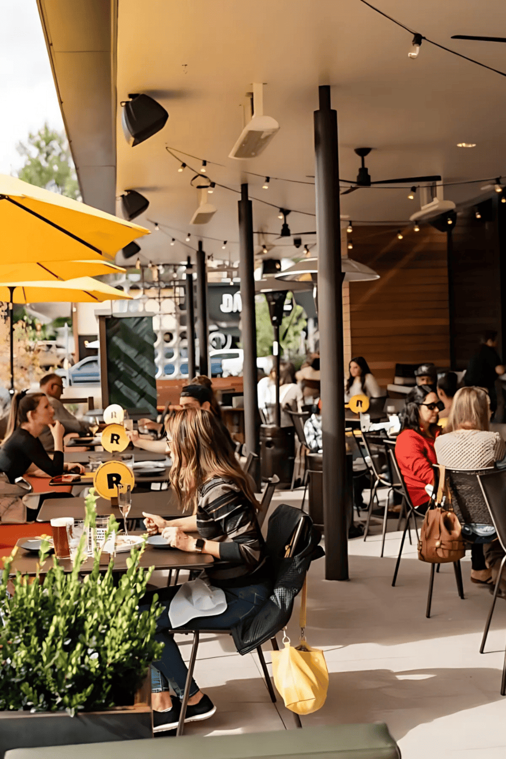 Outdoor restaurant dining with modern decor, string lights, and yellow umbrellas.
