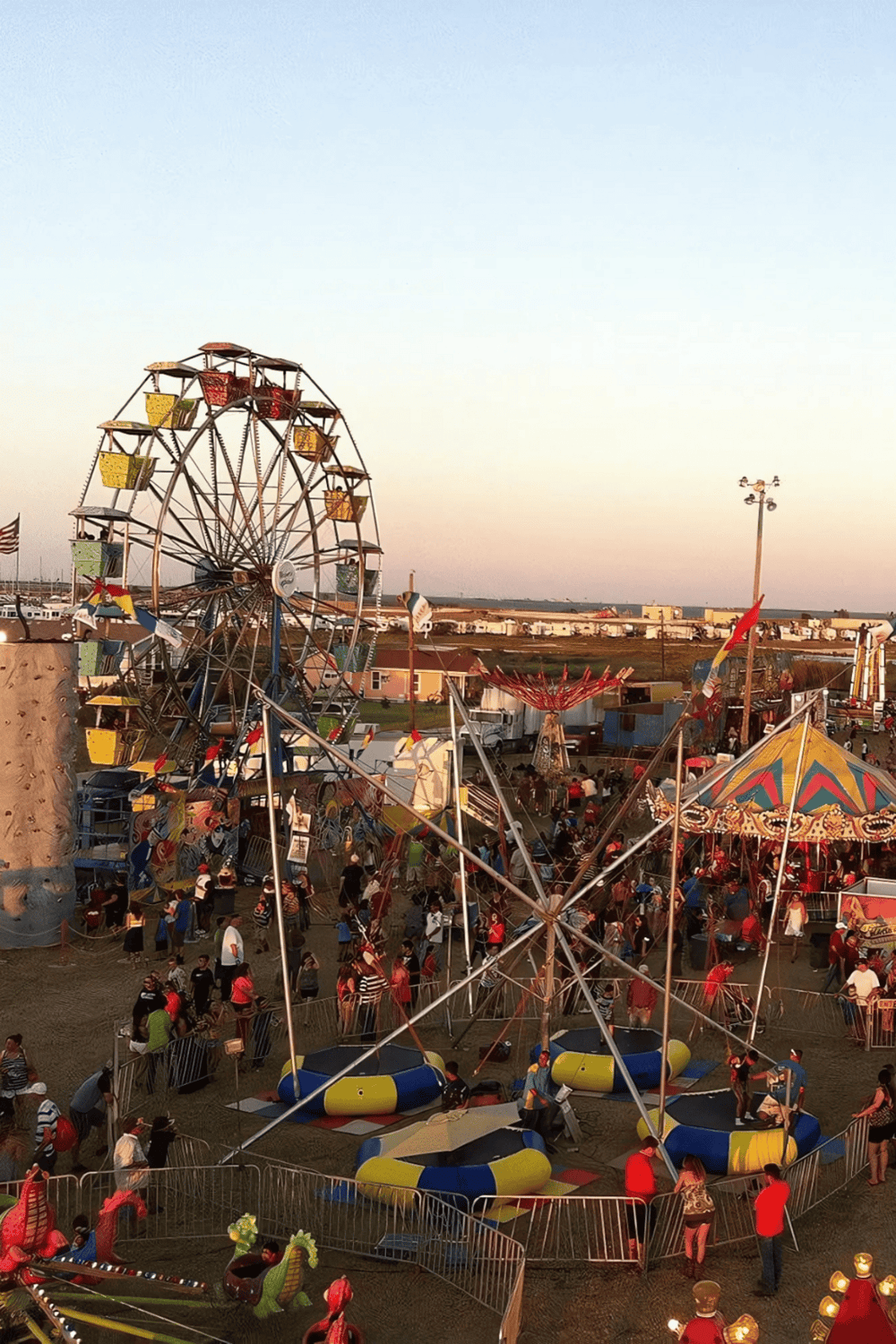 Colorful Ferris wheel at a lively carnival with rides and attractions in the evening.