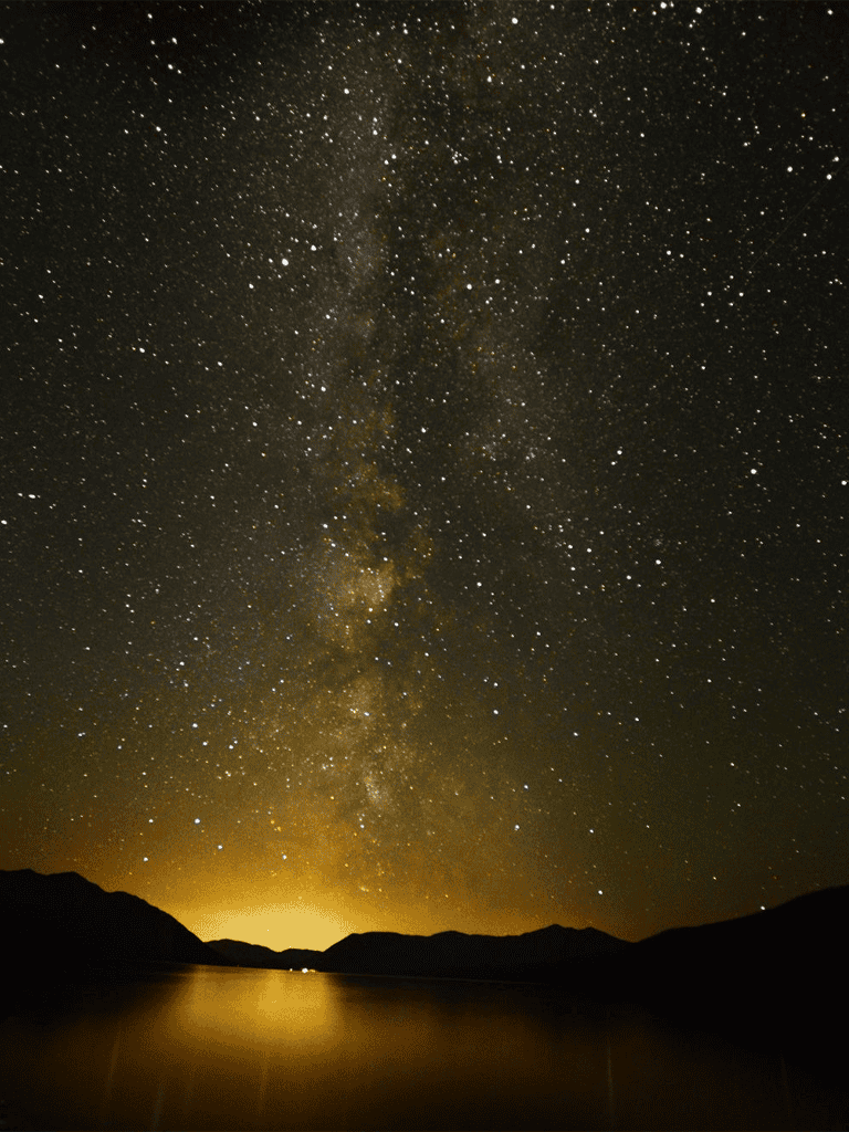 Stargazing under the Milky Way over mountain lake at night, breathtaking celestial view.