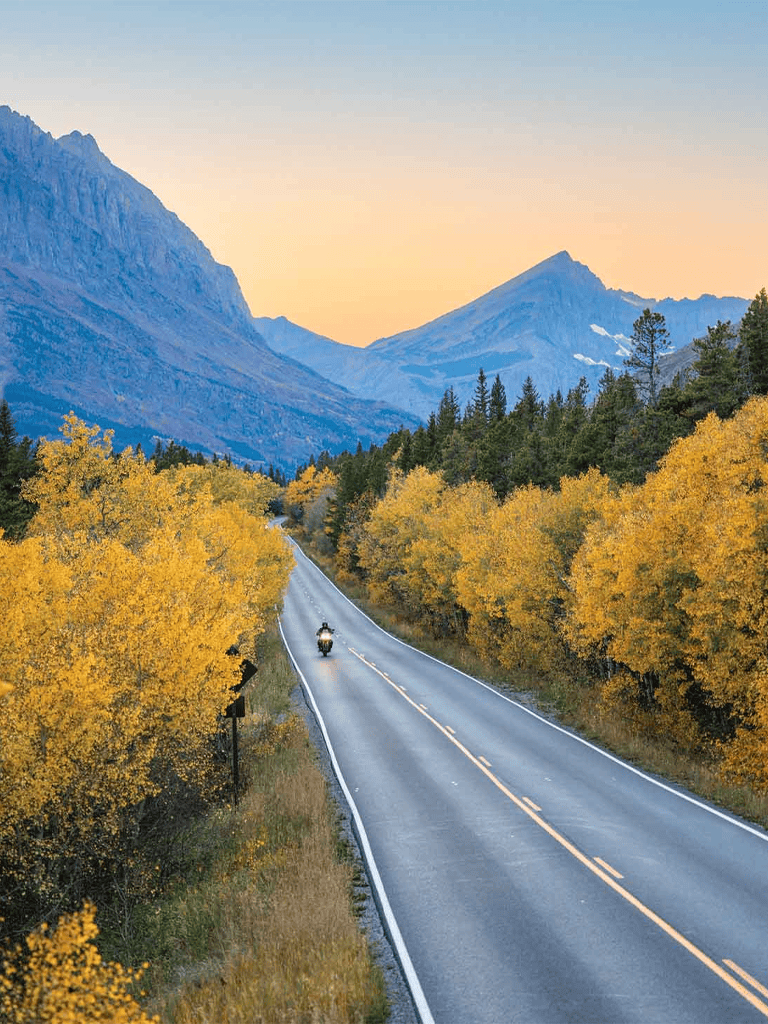 Vast mountain landscape with a winding road and autumn trees during sunset.