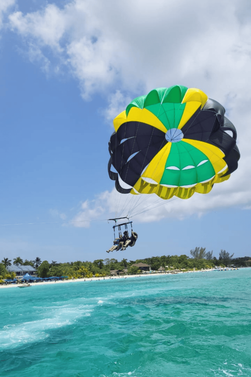 Colorful parasail adventure over clear blue ocean water with tropical shoreline, exciting travel experience.