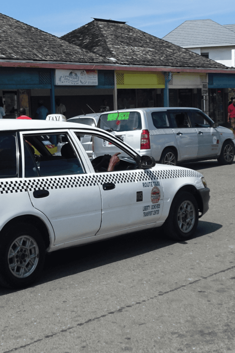 White taxi cab in front of small local shops, street scene in quest for directions.