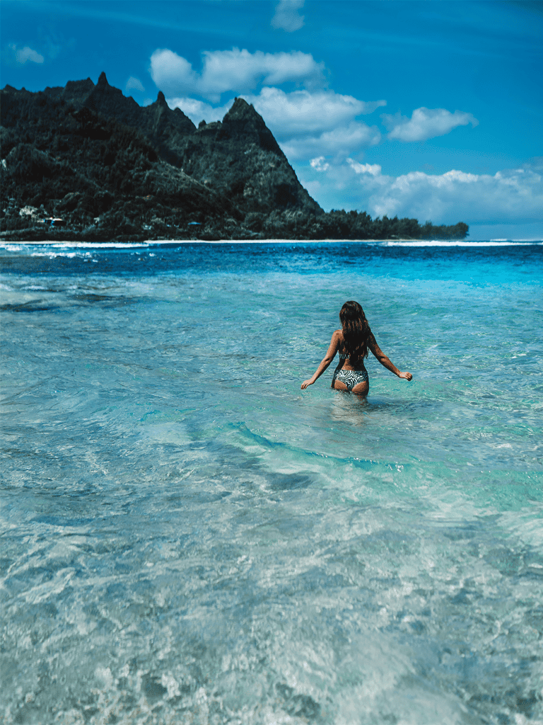 1. Girl swimming in clear ocean water with lush mountains in the background.