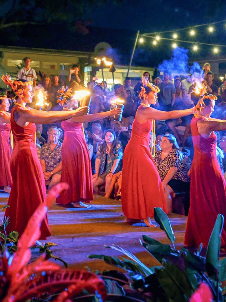 Performers in red dresses holding torches during cultural dance performance at night.