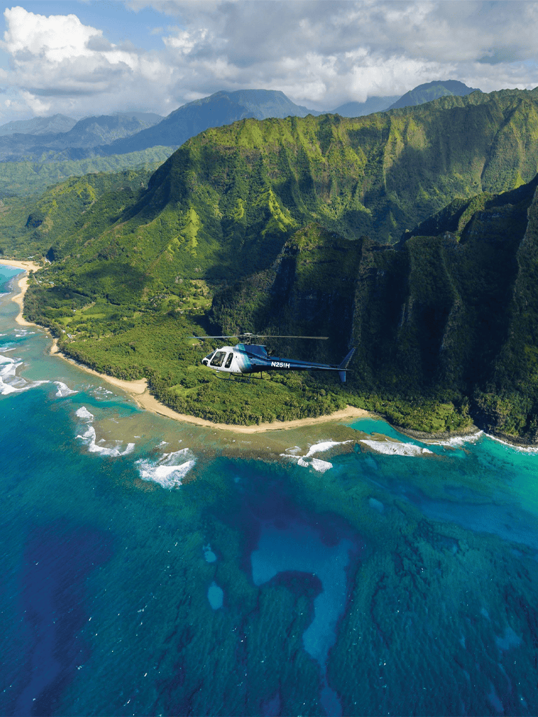 Breathtaking aerial view of lush green mountains and tropical coastline with helicopter flying overhead.