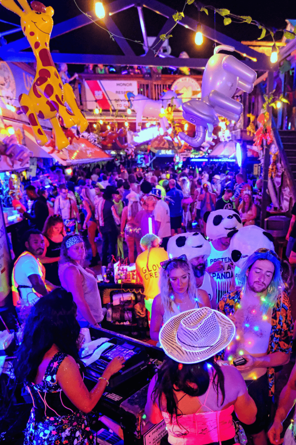 Colorful party scene at QuestForDirections carnival with lively crowd, vibrant decorations, and playful inflatable giraffe and pandas.