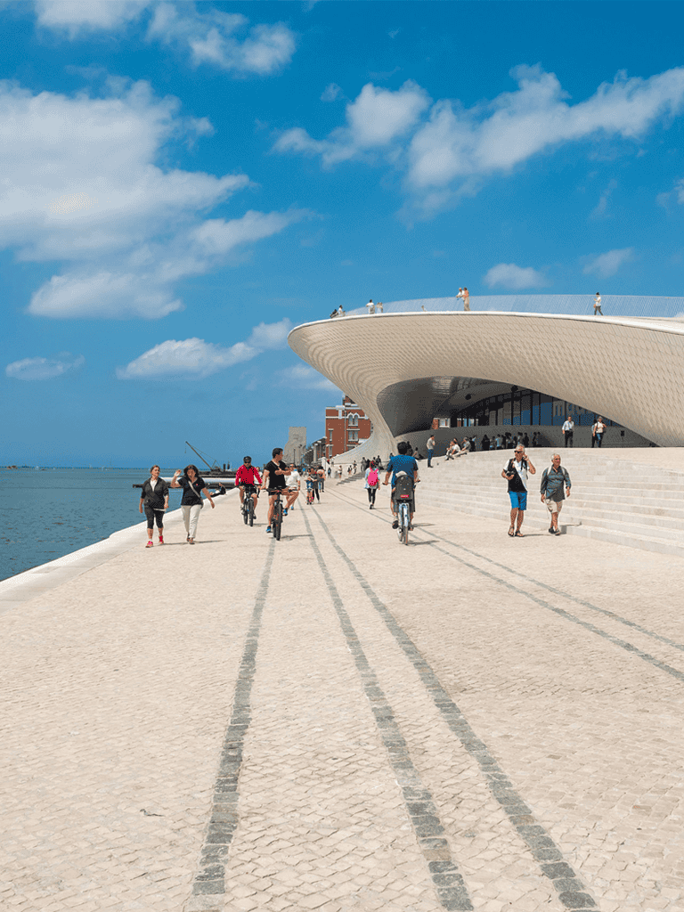 Modern waterfront museum with visitors and cyclers, architectural design, and scenic ocean view.