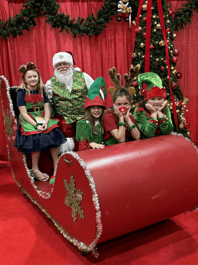 Festive children with Santa Claus at Christmas event, holiday decorations, reindeer hat, elf hat, Christmas tree.