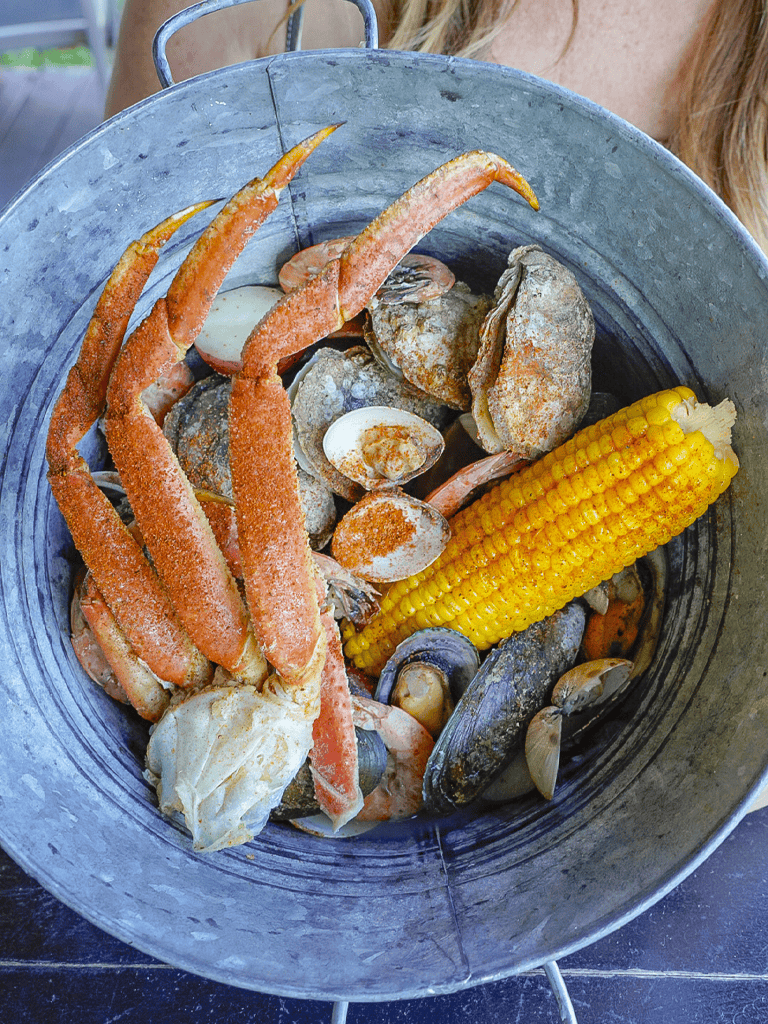 Boiled seafood platter with crab legs, clams, corn, and lobster in a rustic metal bucket.