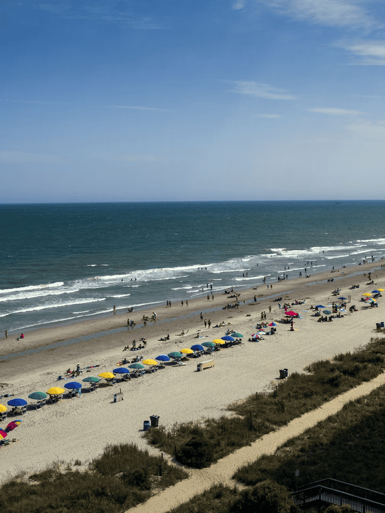 Vibrant beach scene with colorful umbrellas, sandy shores, and ocean waves on a bright sunny day.
