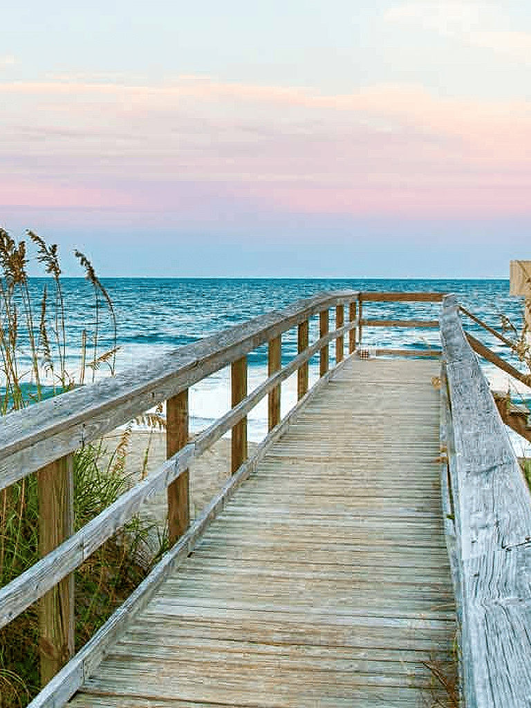 Path to beach over wooden walkway at sunrise or sunset, ocean view, peaceful seaside scenery.