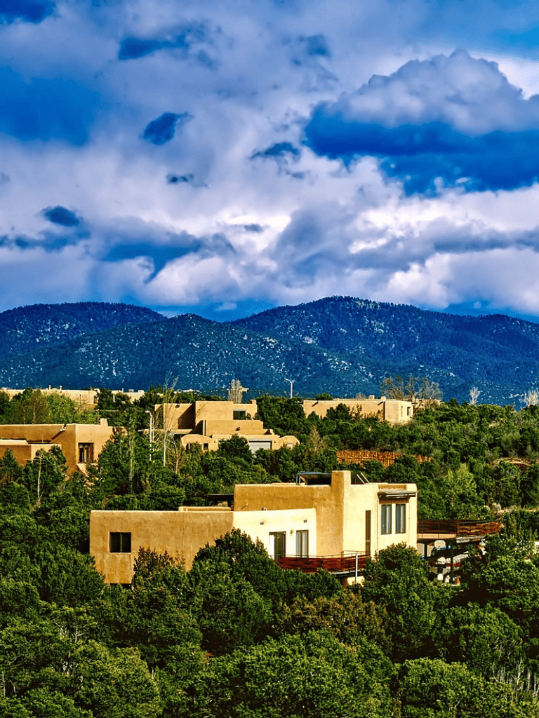 Traditional Southwestern homes in lush greenery under dramatic cloudy sky in Santa Fe.