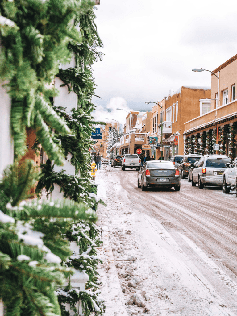 Cozy winter scene in a mountain town with snow-covered streets, colorful buildings, and holiday decorations.