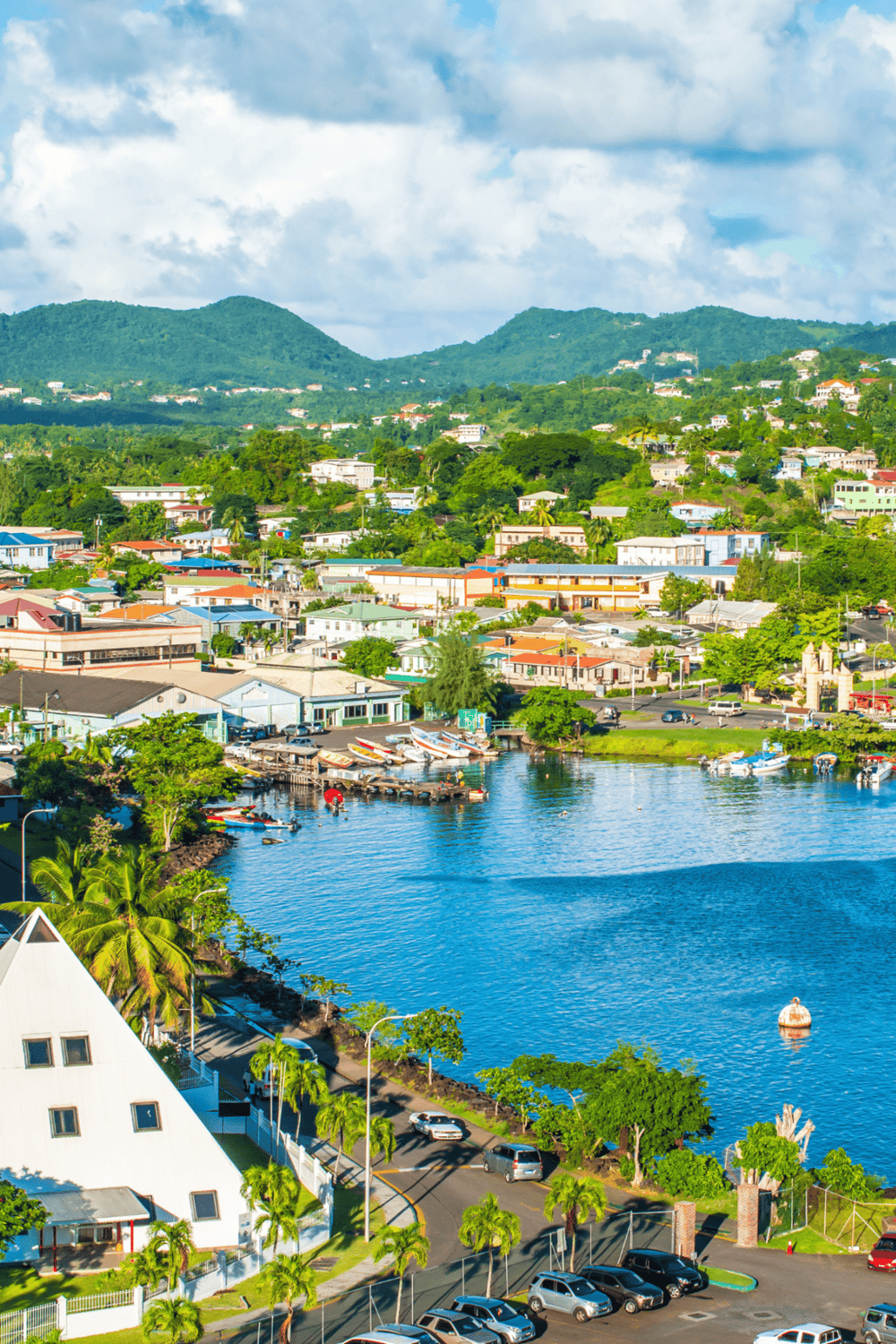 Colorful tropical townscape with waterfront marina and lush green mountains in the background.