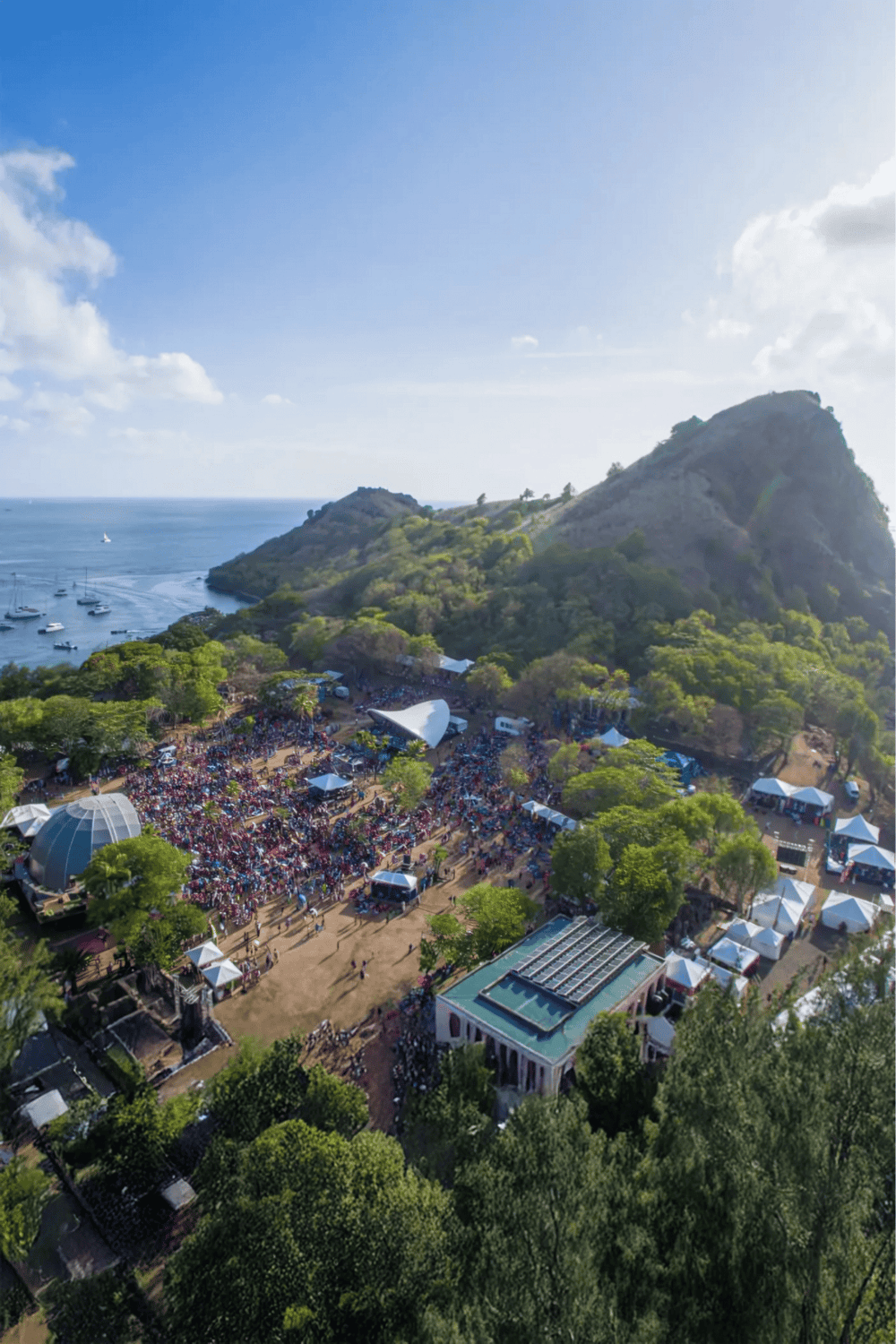 Aerial view of scenic coastal area with mountain, marina, and outdoor event space, showcasing adventure and travel destinations.