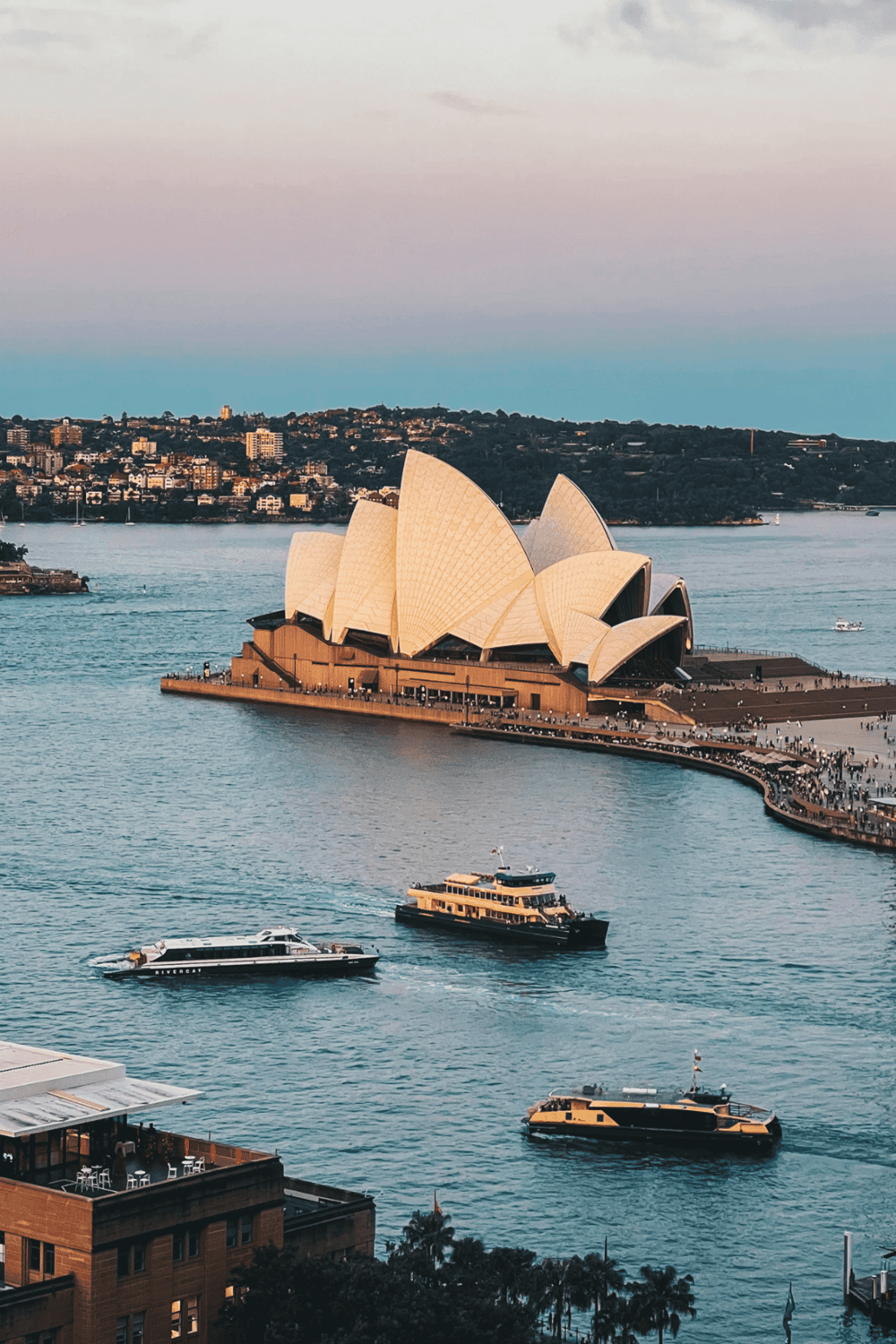 Sydney Opera House on Sydney Harbour with boats and cityscape in the background.