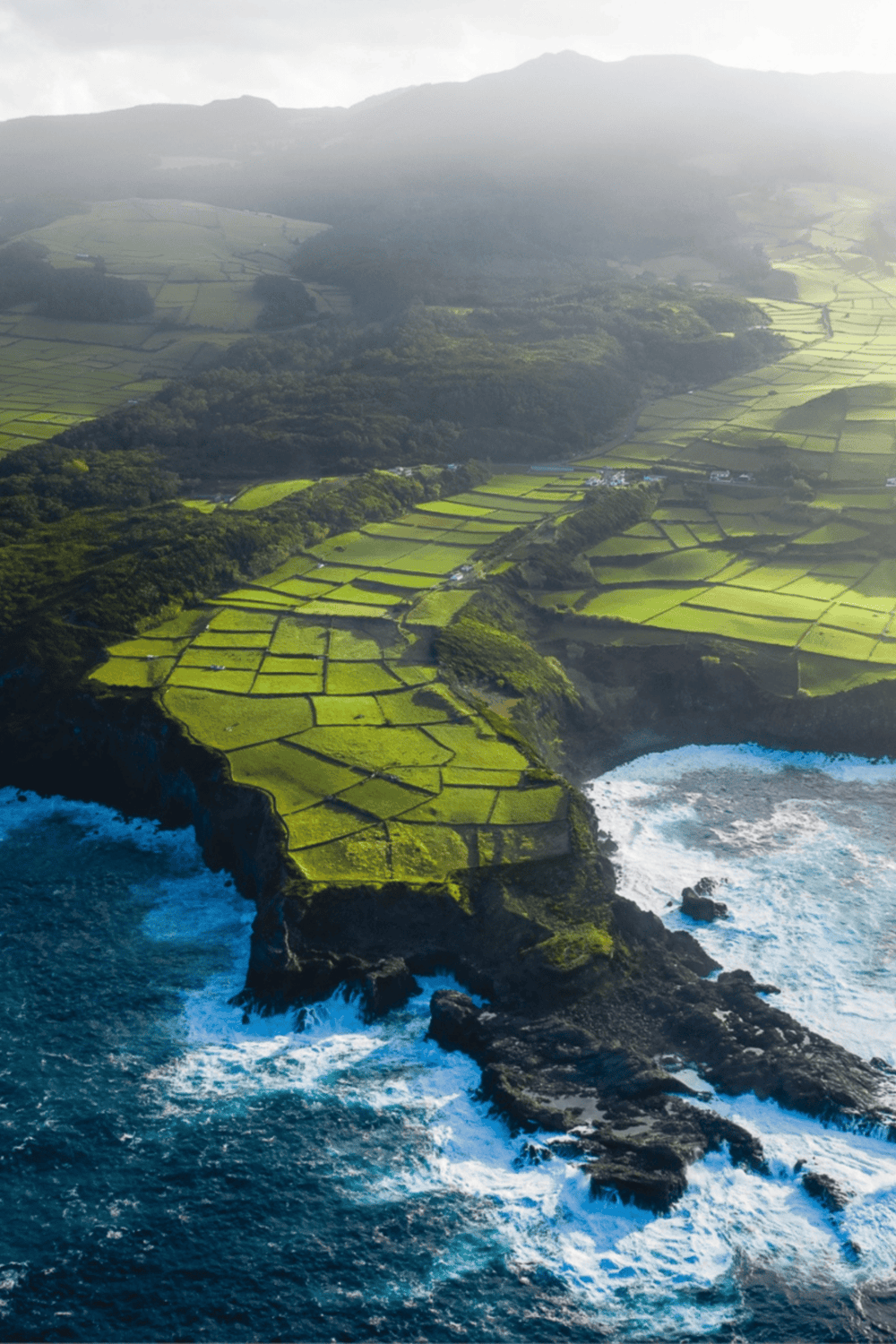 Lush green farmland along rugged coastal cliffs with ocean waves crashing below.