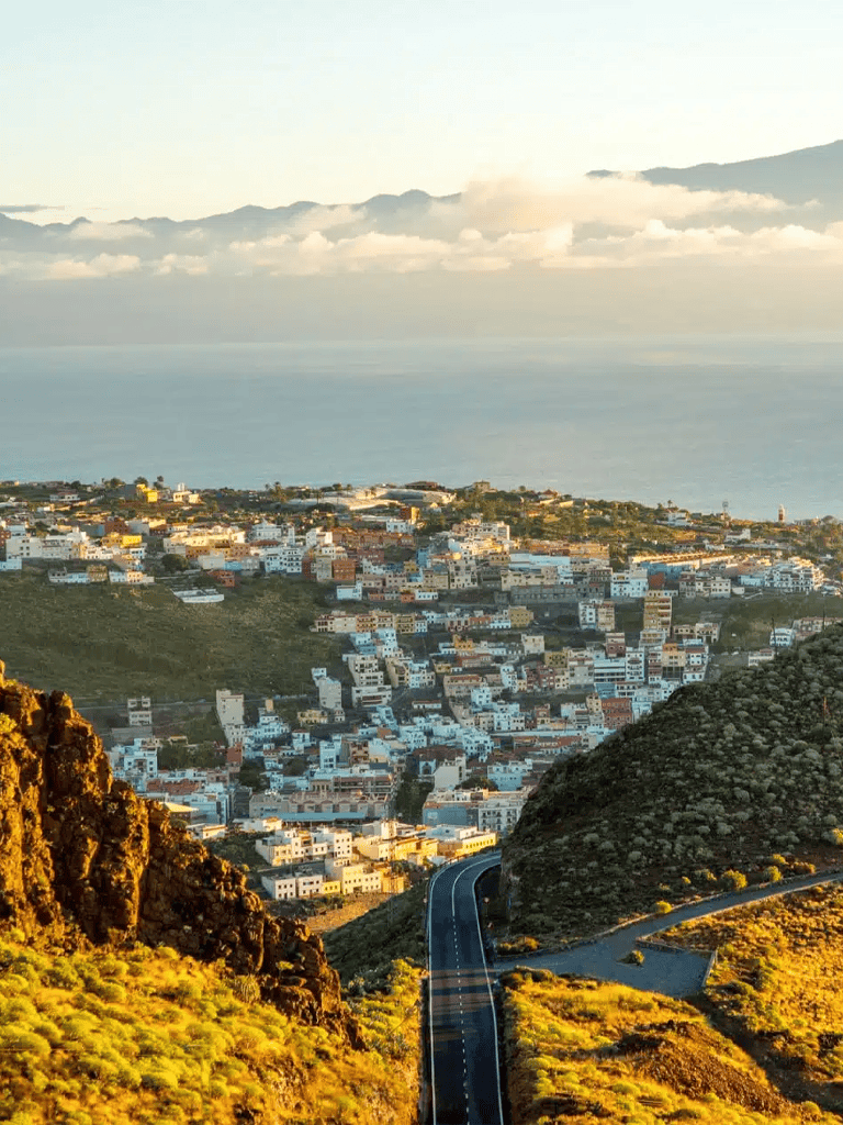 Vibrant coastal cityscape with winding roads and lush hills overlooking the ocean.