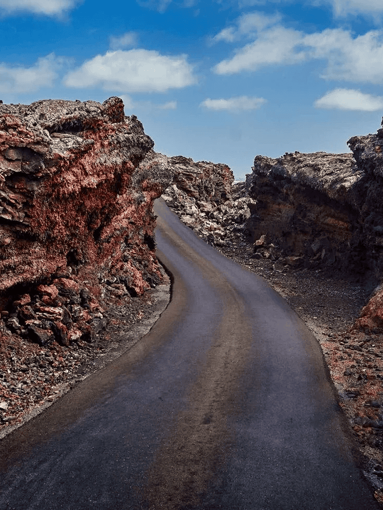 Winding mountain road through rugged volcanic rock formations under blue sky.
