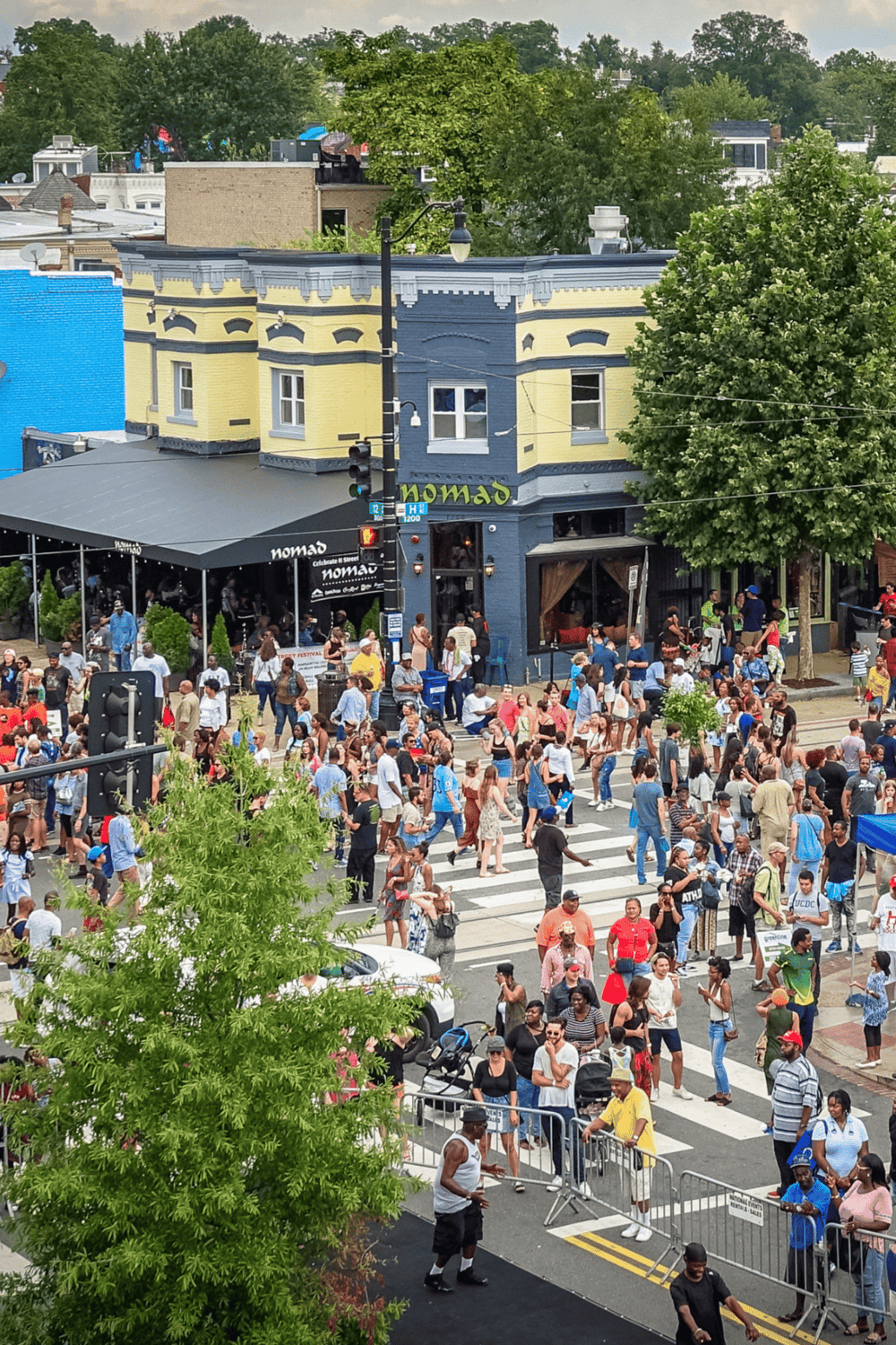 Crowded city street with pedestrians crossing in front of a colorful restaurant building, vibrant urban scene for exploring local dining and entertainment.