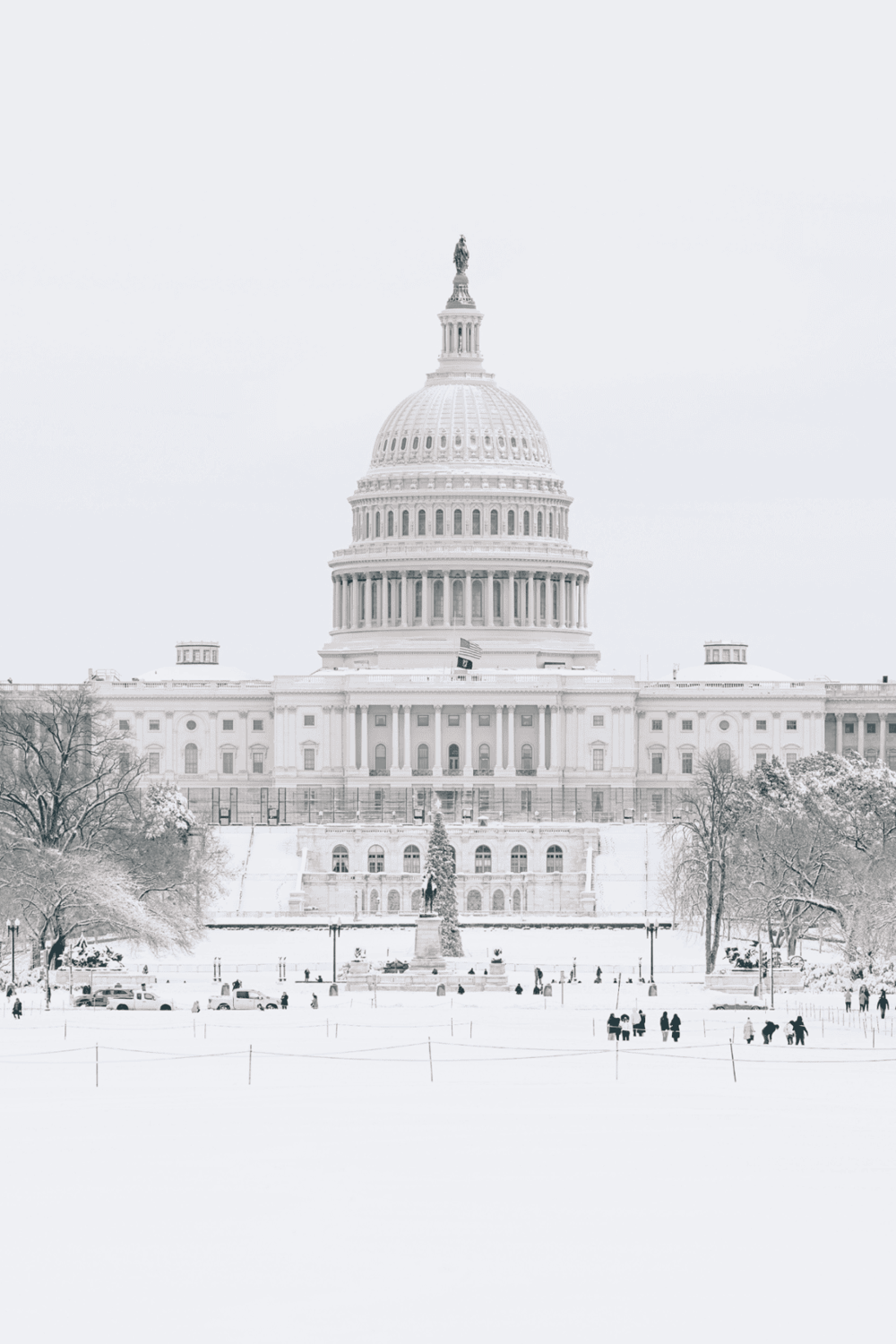 White Capitol building in winter with snow-covered grounds, iconic US government landmark, snow day in Washington DC.