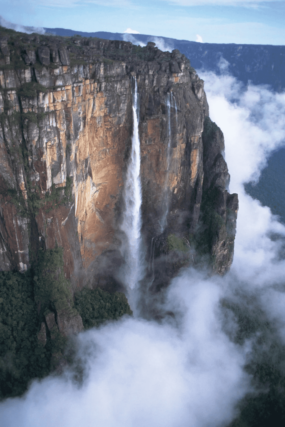 Majestic waterfall cascading down the cliffside surrounded by clouds and lush greenery.