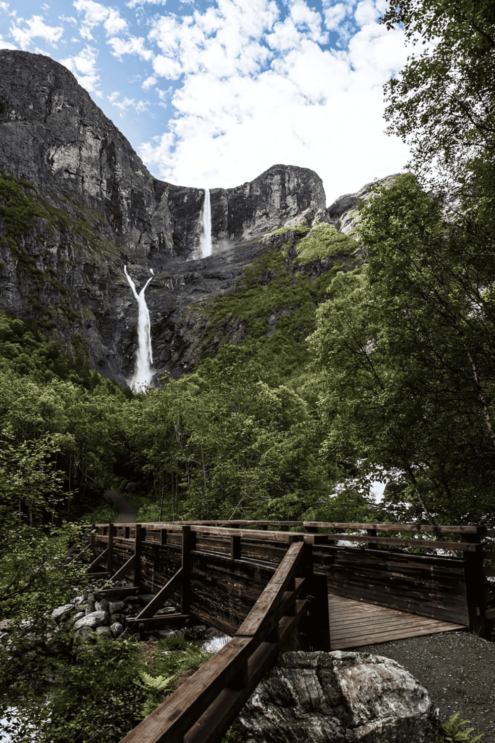 Majestic waterfall in lush green forest with wooden walkway, outdoor scenic nature view.