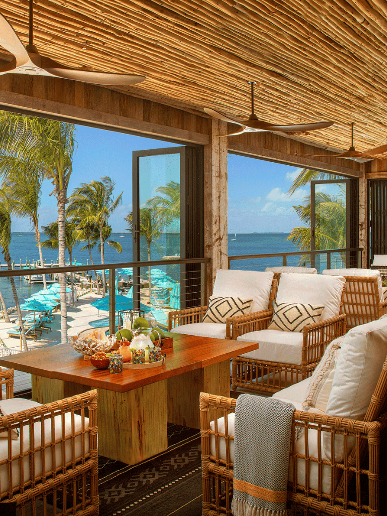 Beachfront tropical resort with patio view of ocean and palm trees.