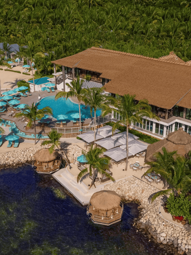 Luxurious tropical resort with pool, thatched cabanas, and scenic ocean views in a lush green setting.