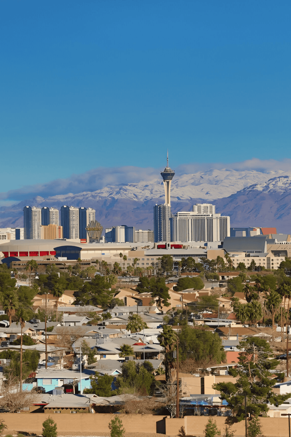 High-rise Las Vegas skyline with Stratosphere Tower and snow-capped mountains in background.