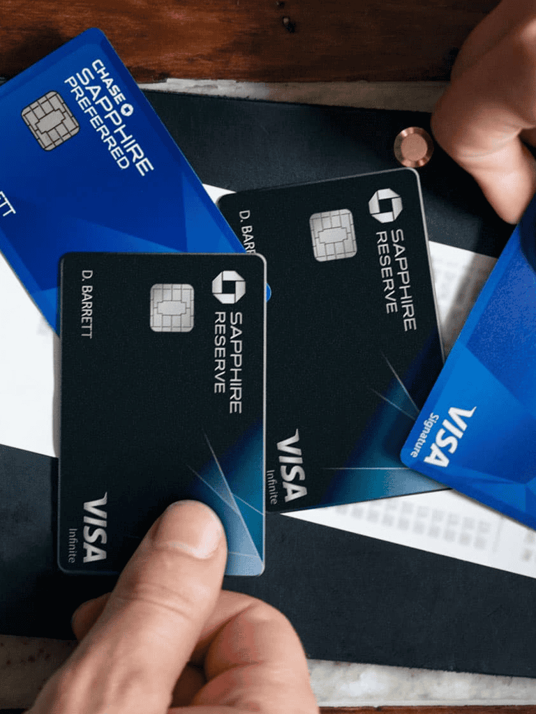 2. Hand holding Visa Sapphire Reserve credit card with other cards on table.