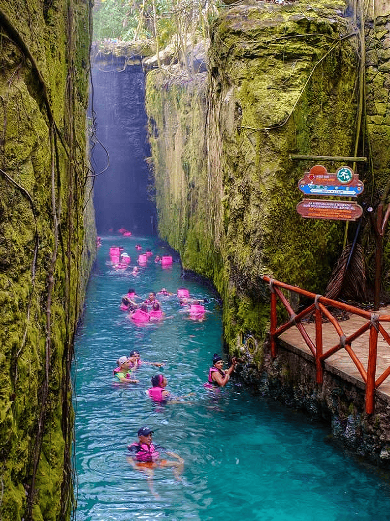 Cold spring water swimming in narrow canyon with lush moss-covered walls and vibrant pink life jackets.