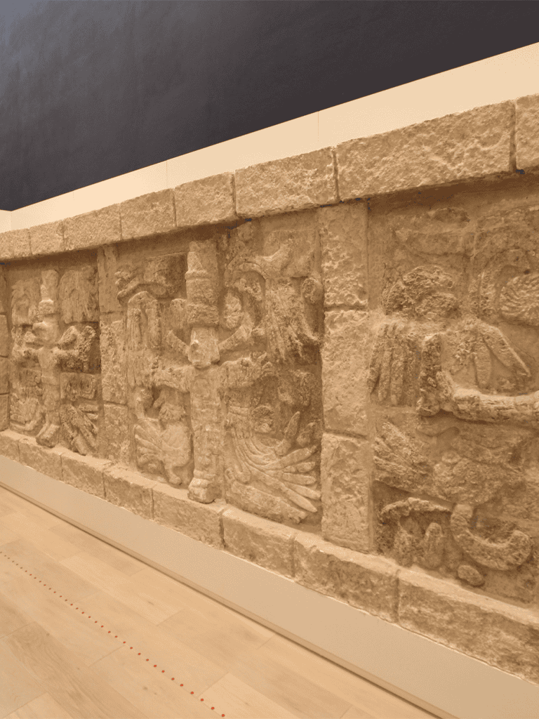 Ancient stone relief sculpture depicting historic figures and scenes, displayed in a modern museum setting.