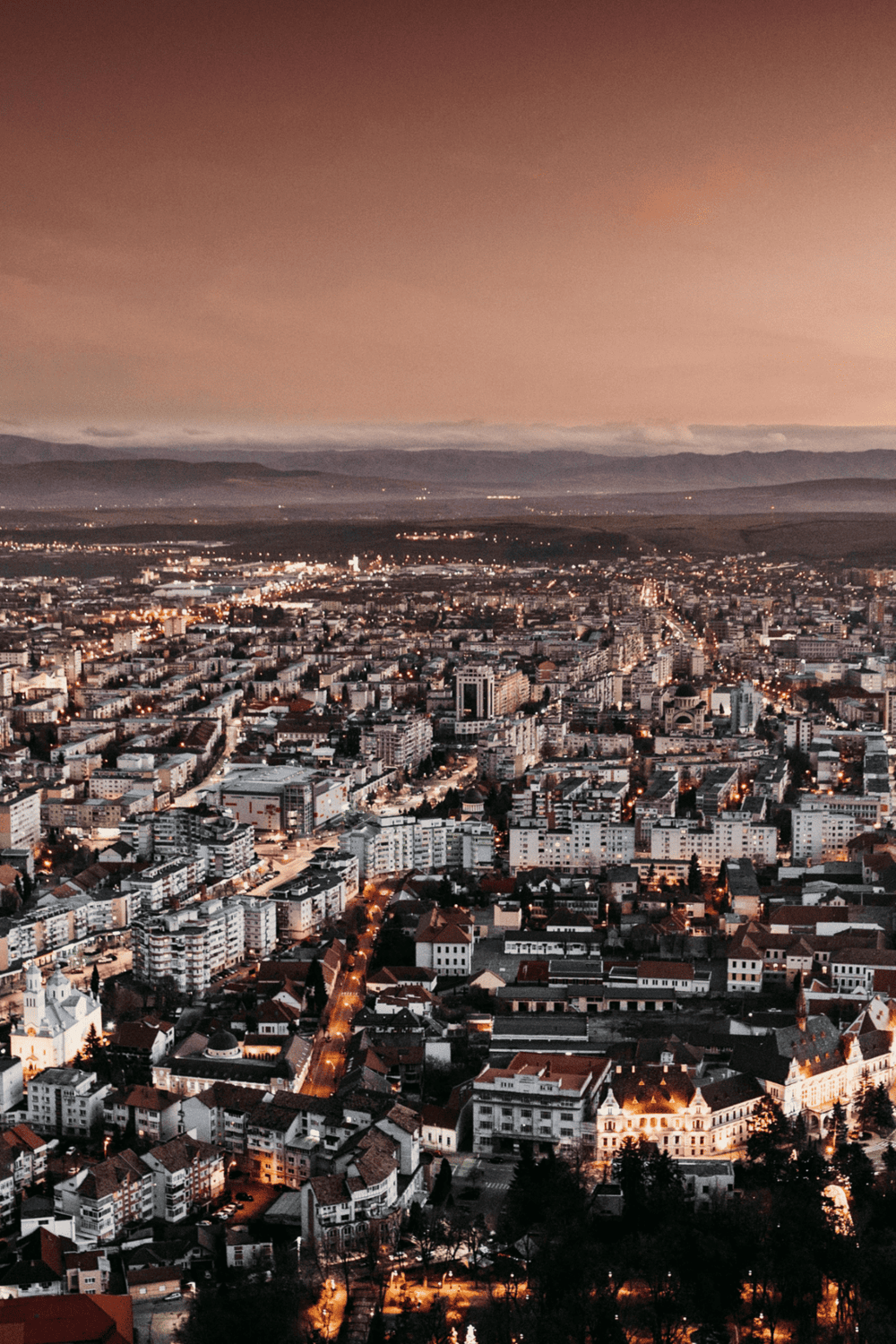 Aerial view of a city skyline at dusk with lit buildings and streets, showcasing urban landscape and city lights.