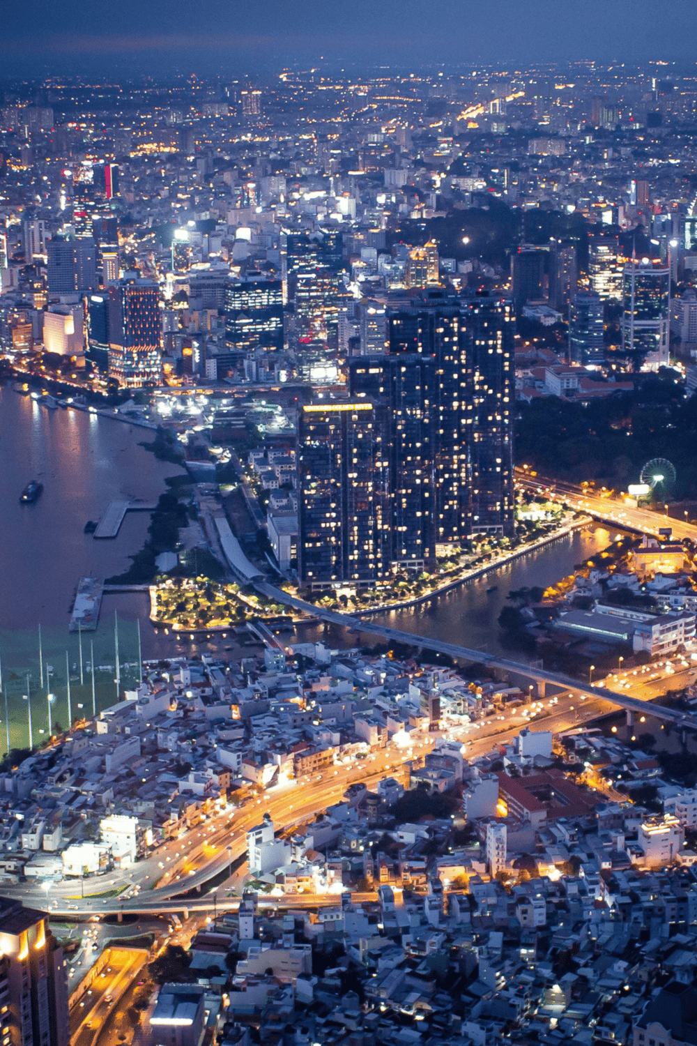 Aerial night view of city skyline with illuminated buildings and bridges over water, showcasing urban navigation and directions.